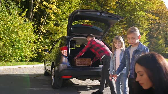 Happy Kids which Helping Their Parents Load the Car's Trunk During their Moving Into New House