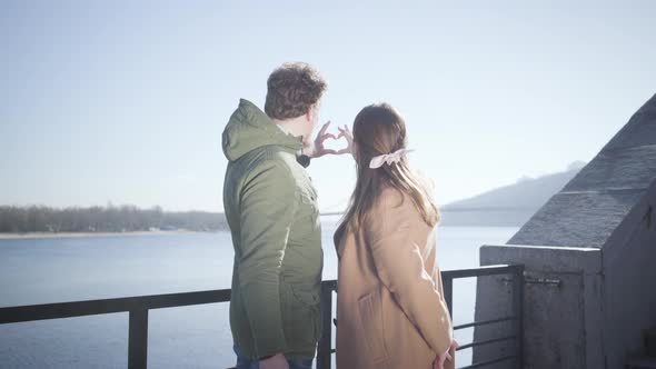 Happy Young Caucasian Man and Woman Making Heart Shape with Hands at the Background of Blue Autumn