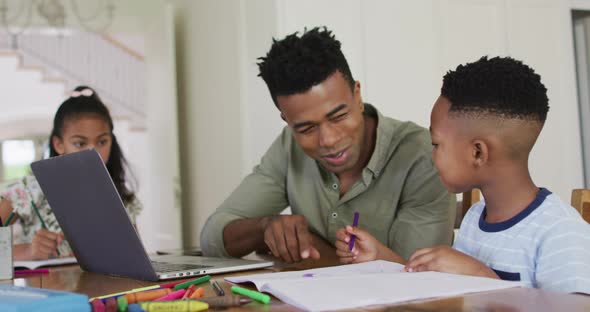 African american father, daugher and son sitting at kitchen table doing homework