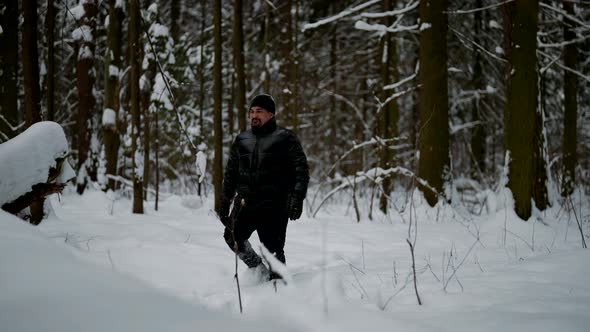 Exhausted Man in Black Cloth is Walking in Snowy Forest Over Snow