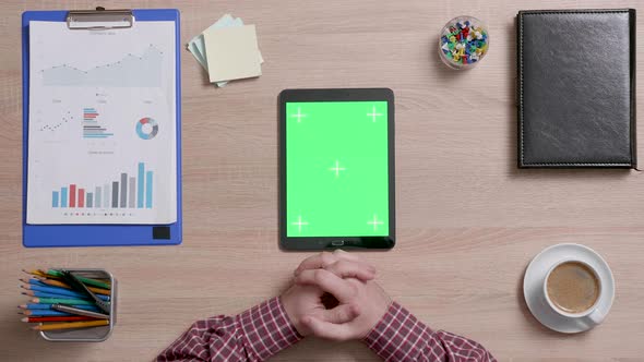 Top View of Male Hands Looking at a Green Screen of a Black Tablet