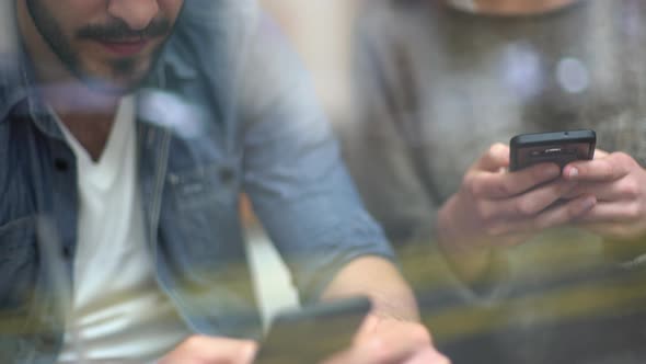 Couple sitting together in cafe window, both using smartphones