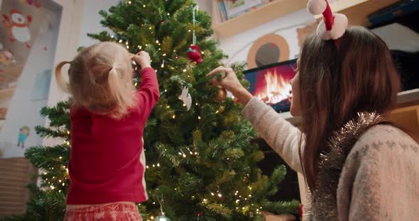 Young Mom with Children Decorate Christmas Tree on Living Room at Evening