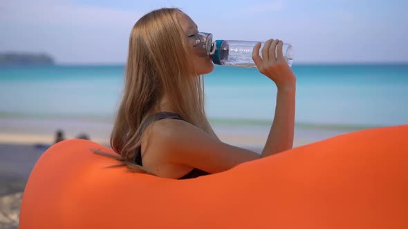 Superslowmotion Shot of a Young Woman on a Tropical Beach Sits on an Inflatable Sofa and Drinks