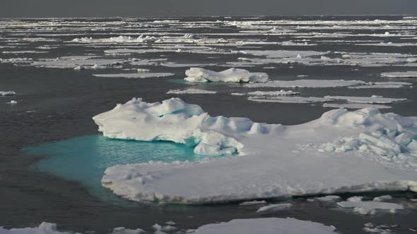 Chunks of Blue Ice Float Past in the Water. Chunks of Ice Under the Snow Are Swaying on the Waves