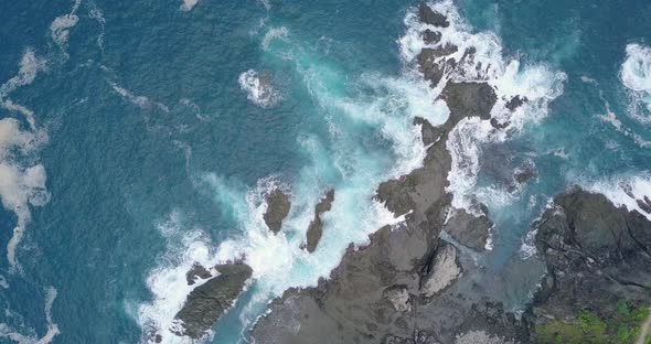 Aerial overhead shot of waves of Indian Ocean hitting boulder and coral reef in the beach in sunny d