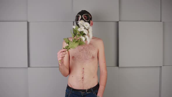 Faceless Shirtless Man in Gas Mask Waving Flowers in Front of Face