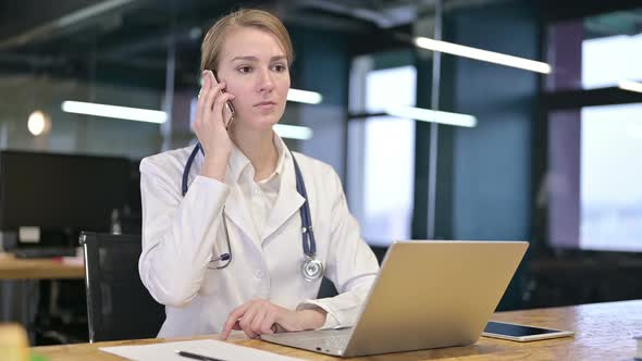 Hardworking Young Female Doctor Talking on Smartphone in Office 