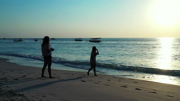 Silhouette of girls exercising acrobatic figures on sandy beach, taking photos of friend at sunset o