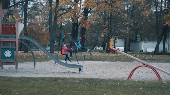 Brother and Sister Enjoying the Playground in Park at Autumn Day Riding on a Swing and Having Fun.