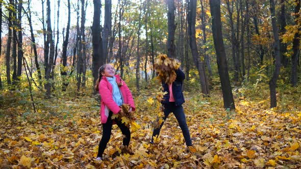 Two Little Girls Throw Autumn Leaves in the Park