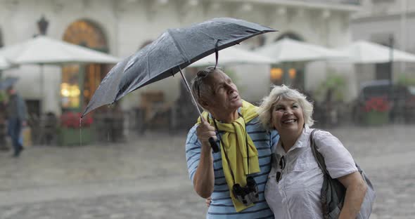 Happy Senior Tourists Stand Downtown and Enjoy the Rainy Weather in Lviv