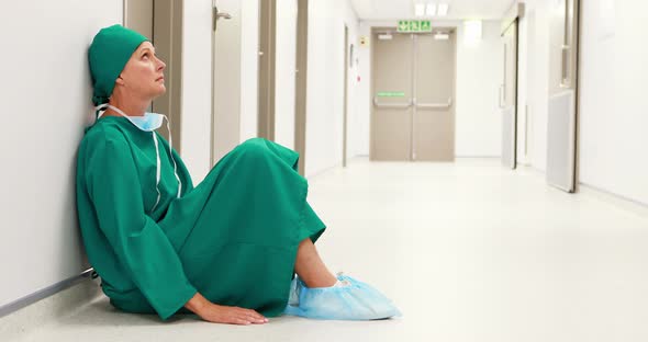 Tensed female surgeon sitting in corridor