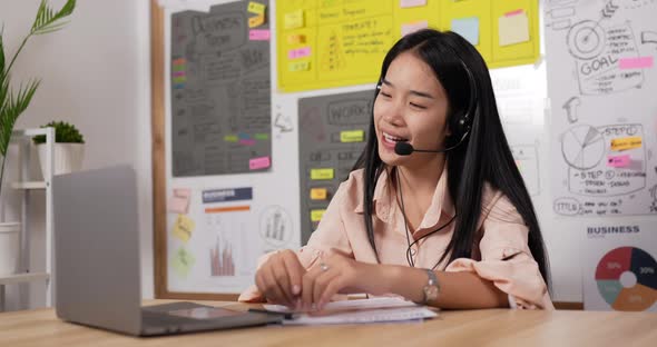 Asian woman with headset using laptop and talking