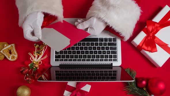 Top View Santa Hands in White Gloves are Typing on Keyboard Laptop By Red New Year Decorated Table