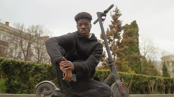 A Young AfricanAmerican Man in a Black Sweater and Black Jeans and Sneakers Sits on an Electric