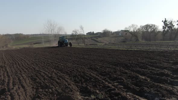 Wide Shot of Agricultural Tractor Furrowing Fertile Field on Sunny Spring Day