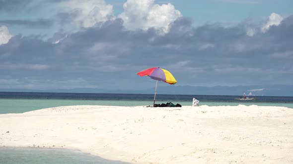 red blue and yellow beach umbrella blowing in the wind on a tropical white sandy beach island as Fil