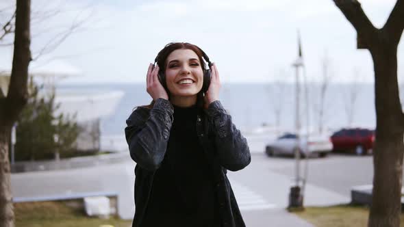 Attractive Young Brunette Girl with Black Wireless Headphones on is Walking Somewhere Listening and