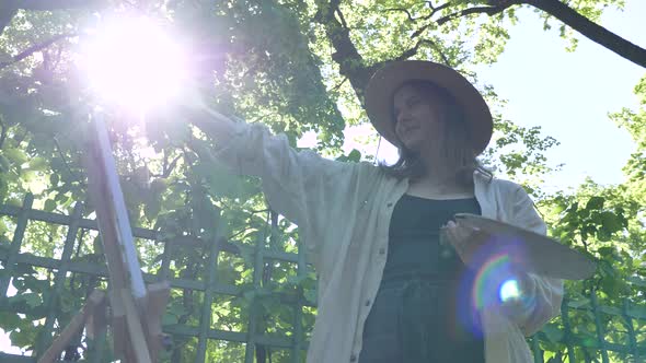 Young Woman Painter in Straw Hat and Shirt Paints By Lilac