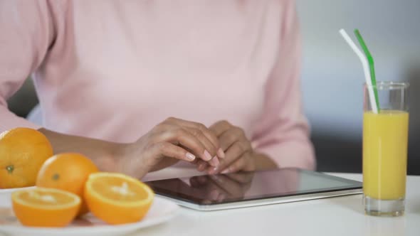 Girl Typing on Tablet Oranges and Fresh Juice on Table Blogging About Dieting