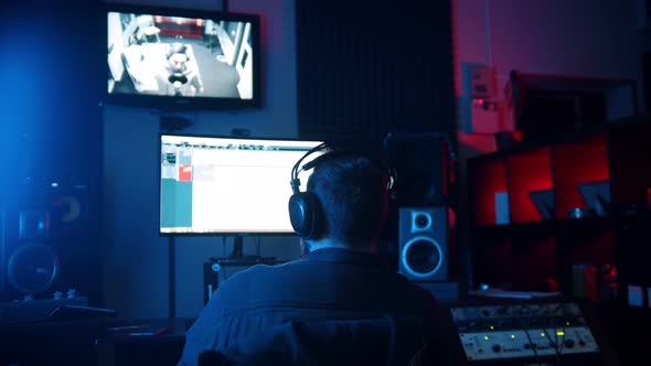 A Man Sound Engineer in Headphones Working in the Neon Sound Recording Studio - Recording a Rap