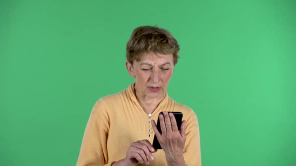 Portrait of Elderly Woman Is Talking for Video Chat Using Mobile Phone Isolated Over Green