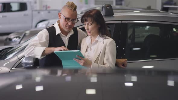 Successful Caucasian Married Couple Examining New Vehicle Features on Tablet Standing in Car