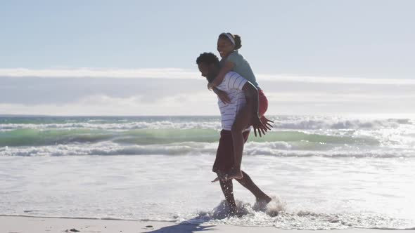 African american man smiling and carrying african american woman piggyback on the beach