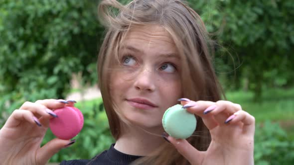 Young blond girl is looks at macaroons and does not know which one to choose