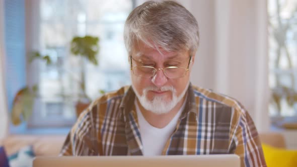 Senior Man Wearing Glasses Using Computer in Living Room