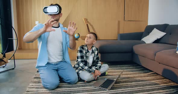 Modern Smart Father in Virtual Reality Headset Moving Hands on Imaginary Screen While His Son