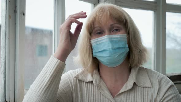 Portrait Of Mature Woman In Medical Mask On Her Face At Window