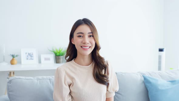 Portrait of Asian beautiful woman sit on sofa in living room at home smile, look at camera.