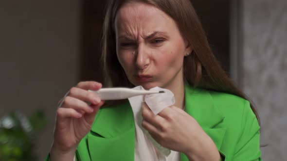 Sick Woman Looks at Thermometer Wiping Nose with Napkin