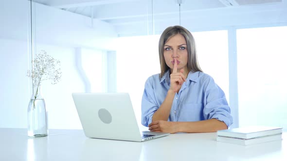 Young Woman Gesturing  Silence in office, Finger on Lips