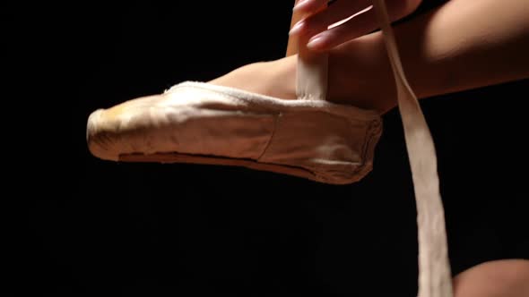 Closeup Unrecognizable Ballerina Putting on Tying Pointies at Black Background