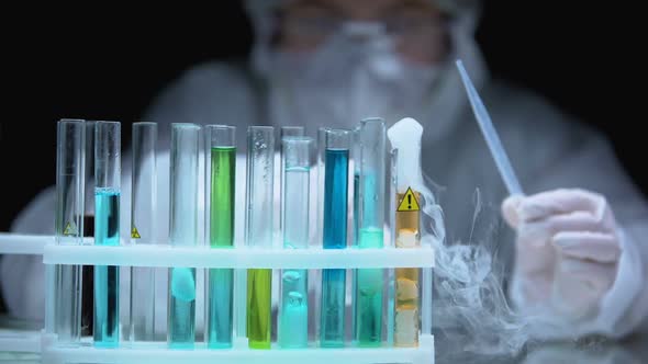 Scientist Dropping Sample to Liquid Boiling in Test Tube With Warning Symbol