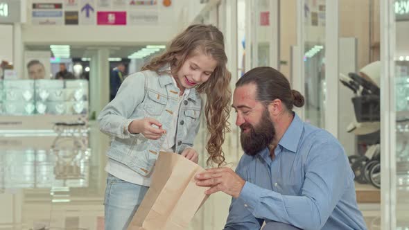 Cute Little Girl and Her Father Looking Inside Shopping Bags at the Mall