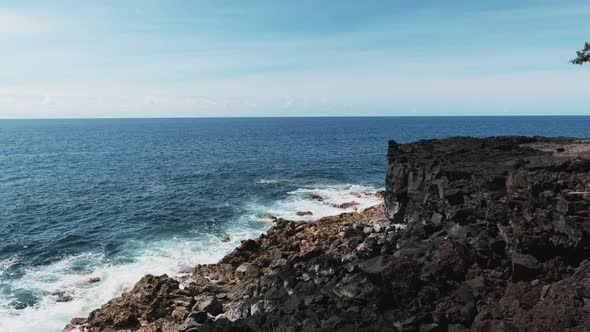 Blue waves of Pacific Ocean break against basalt cliff, Hawaii.