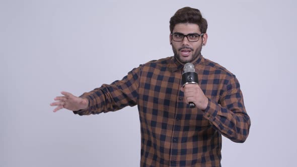 Happy Young Bearded Indian Hipster Man Presenting Something with Microphone