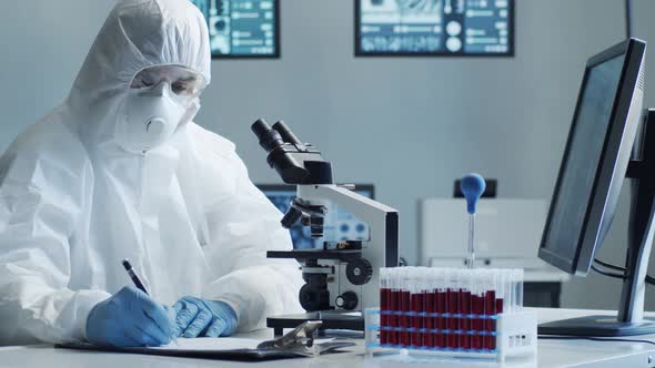 Scientist in protection suit and masks working in research lab using laboratory equipment.