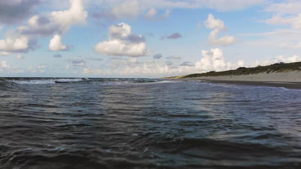 AERIAL: Flying very low over crashing waves above green sea water on a sunny day near the coast