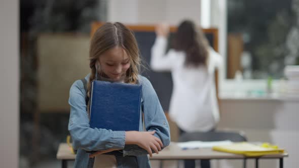 Charming Smart Caucasian Schoolgirl Closing Workbook and Smiling Looking at Camera