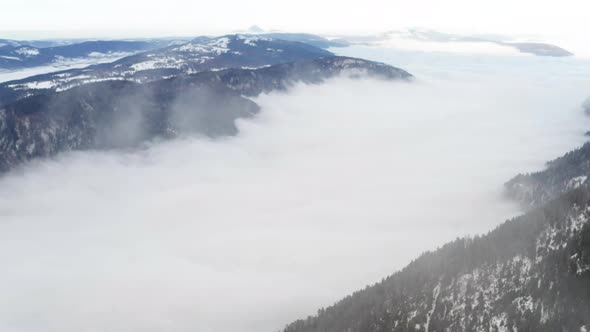 Drone flying through thin clouds above a cloud covered valley