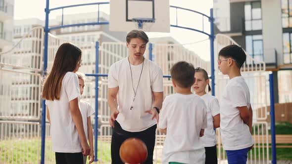 Basketball Coach Shows School Kids How to Throw the Ball Into the Basket on Basket Court