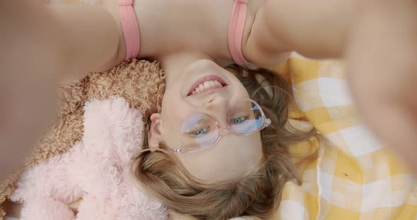 the Girl with Pink Glasses Makes Herself Smiling at Sea on a Yellow Blanket