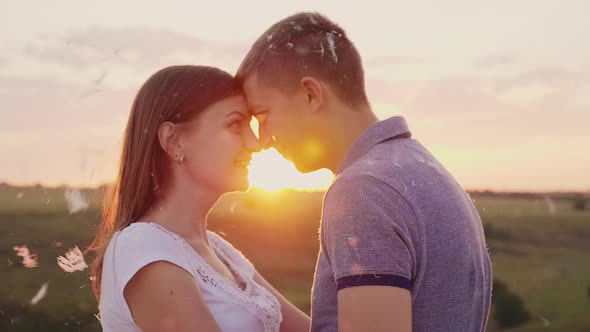 A Couple in Love Lies Facing Each Other at Sunset. Around Fly Feathers After the Fight with Pillows