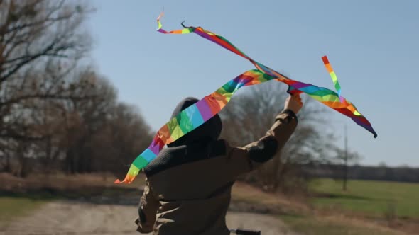 A Happy Boy with a Flying Rainbow Kite Rides a Bicycle on the Road