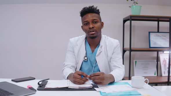 Doctor Sits at the Desk and Talk to Camera Wearing Medical Gown and Stethoscope